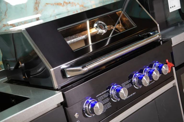 Close view of a built-in outdoor kitchen grill with control knobs and hood thermometer