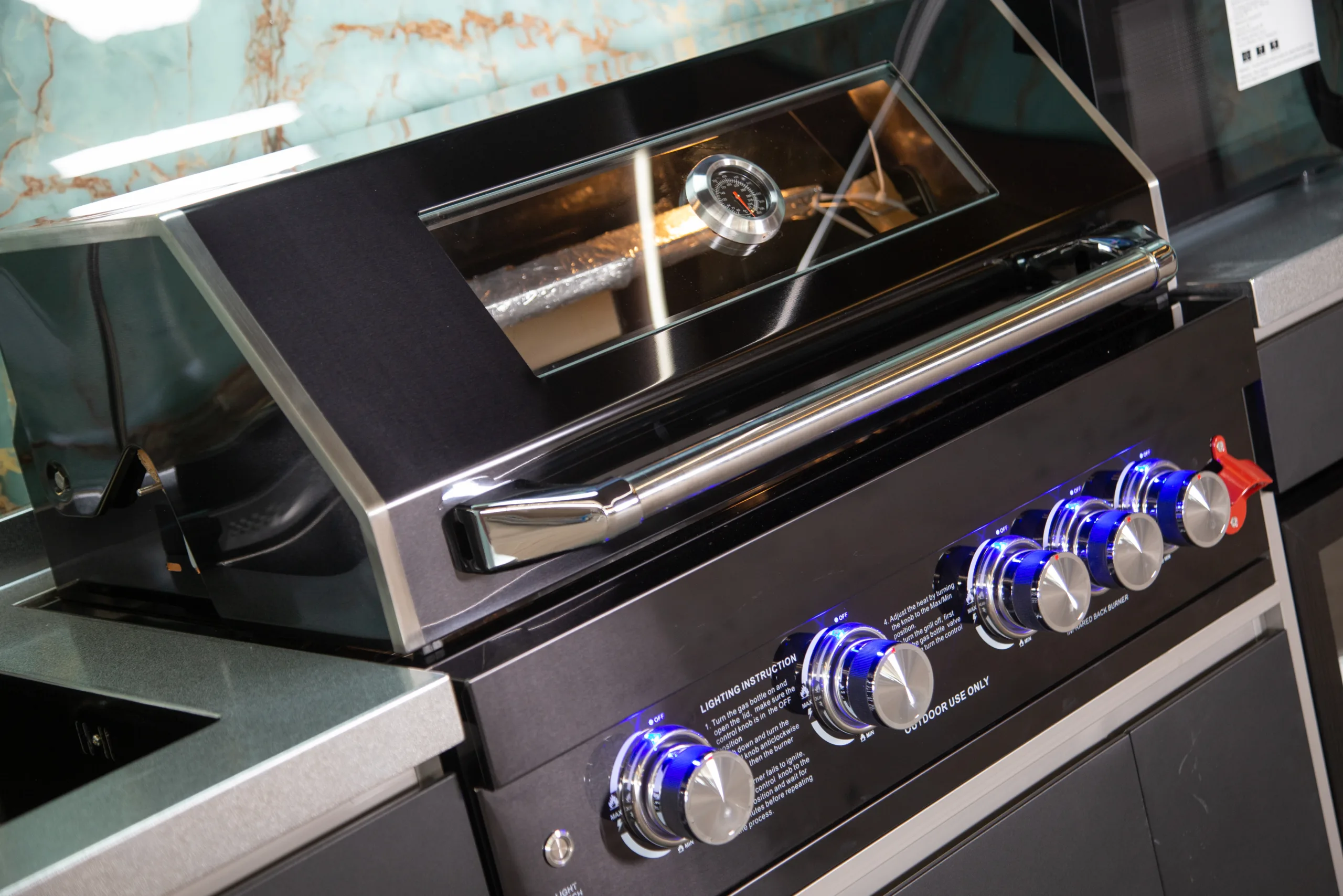 Close view of a built-in outdoor kitchen grill with control knobs and hood thermometer