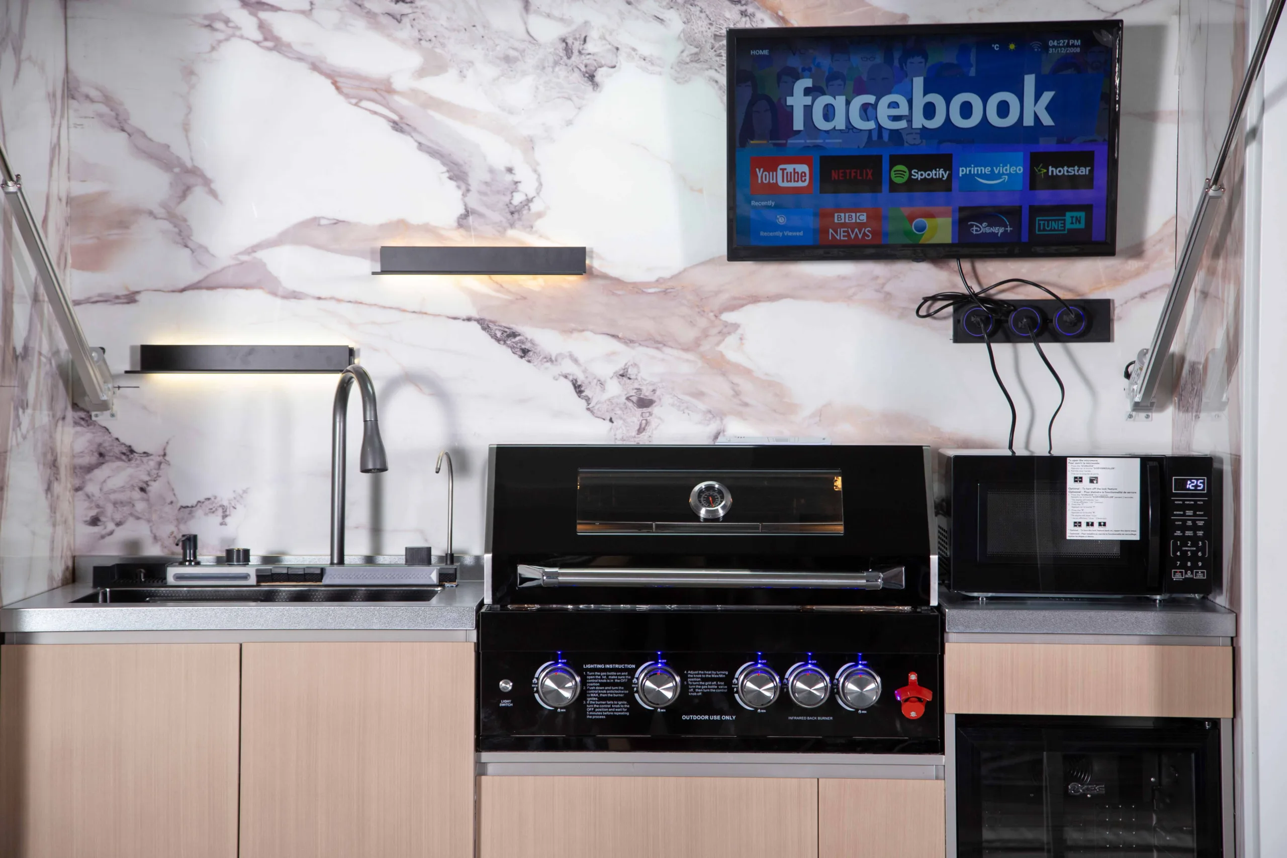 Covered outdoor kitchen with grill, sink, refrigerator, microwave, lighting, and television
