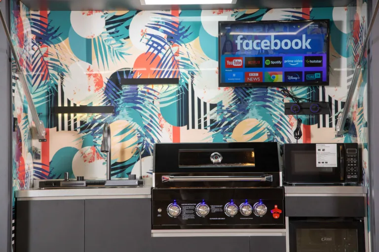 Outdoor kitchen with colorful tropical-pattern backsplash, grill, sink, refrigerator, television, and lighting
