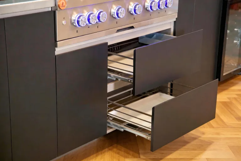 Pull-out baskets and drawers below a grill in a dark outdoor kitchen cabinet